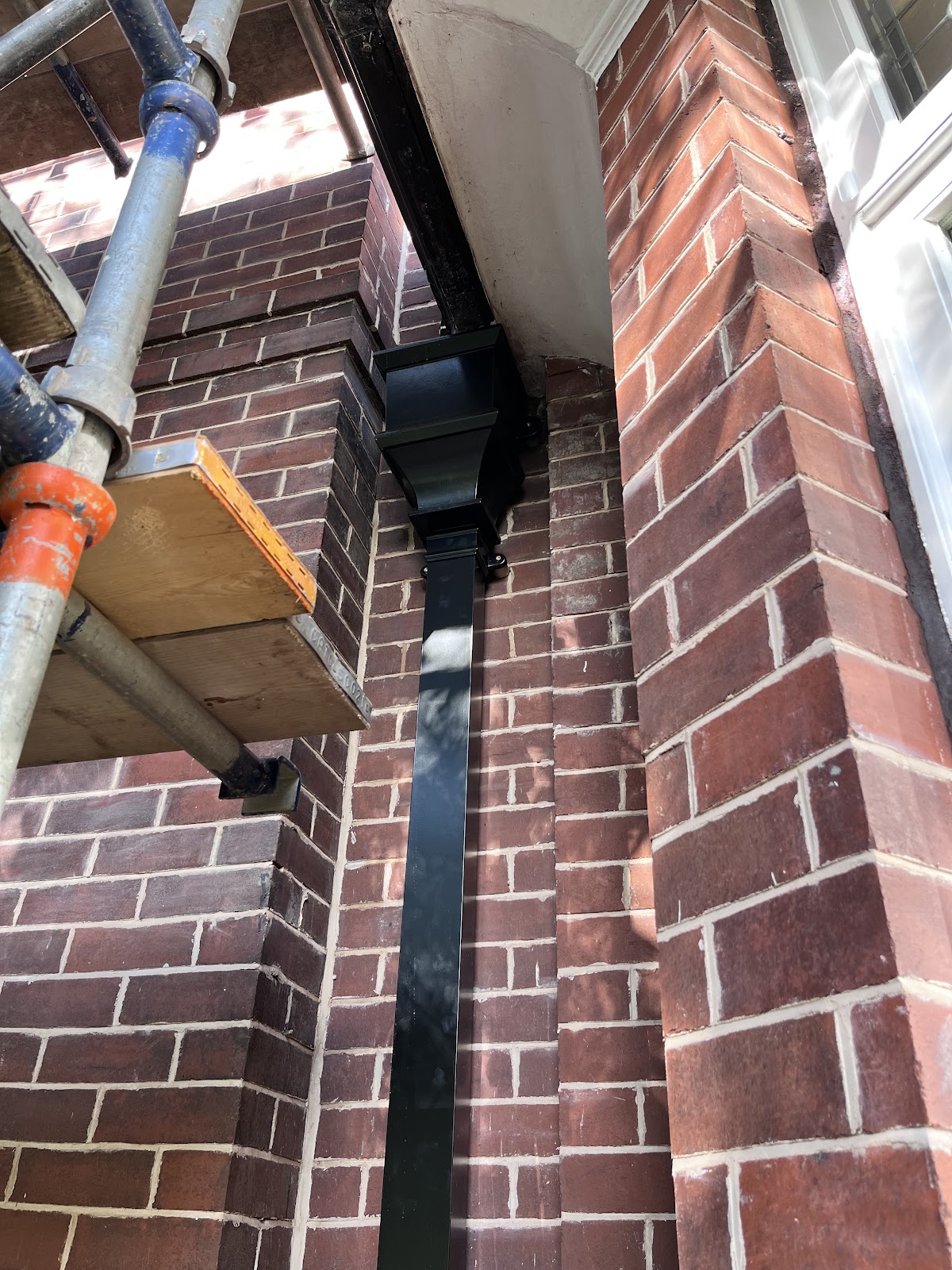 New black downpipe and hopper fitted to brickwork
